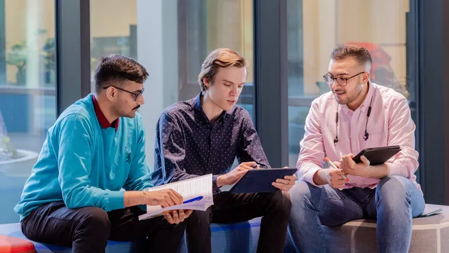 Three students in the seating areas in the gallery of the new EI building on the TUM Campus Garching
