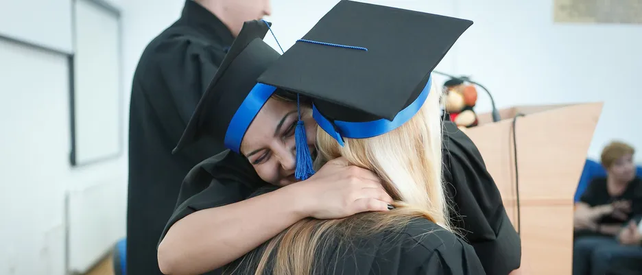 Graduate Zwei Frauen mir Doktorhut umarmen sich